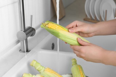 Woman washing corn cob in kitchen, closeup