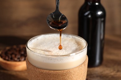 Photo of Pouring syrup into glass of tasty coffee on table, closeup