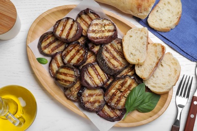 Delicious grilled eggplant slices served on white wooden table, flat lay
