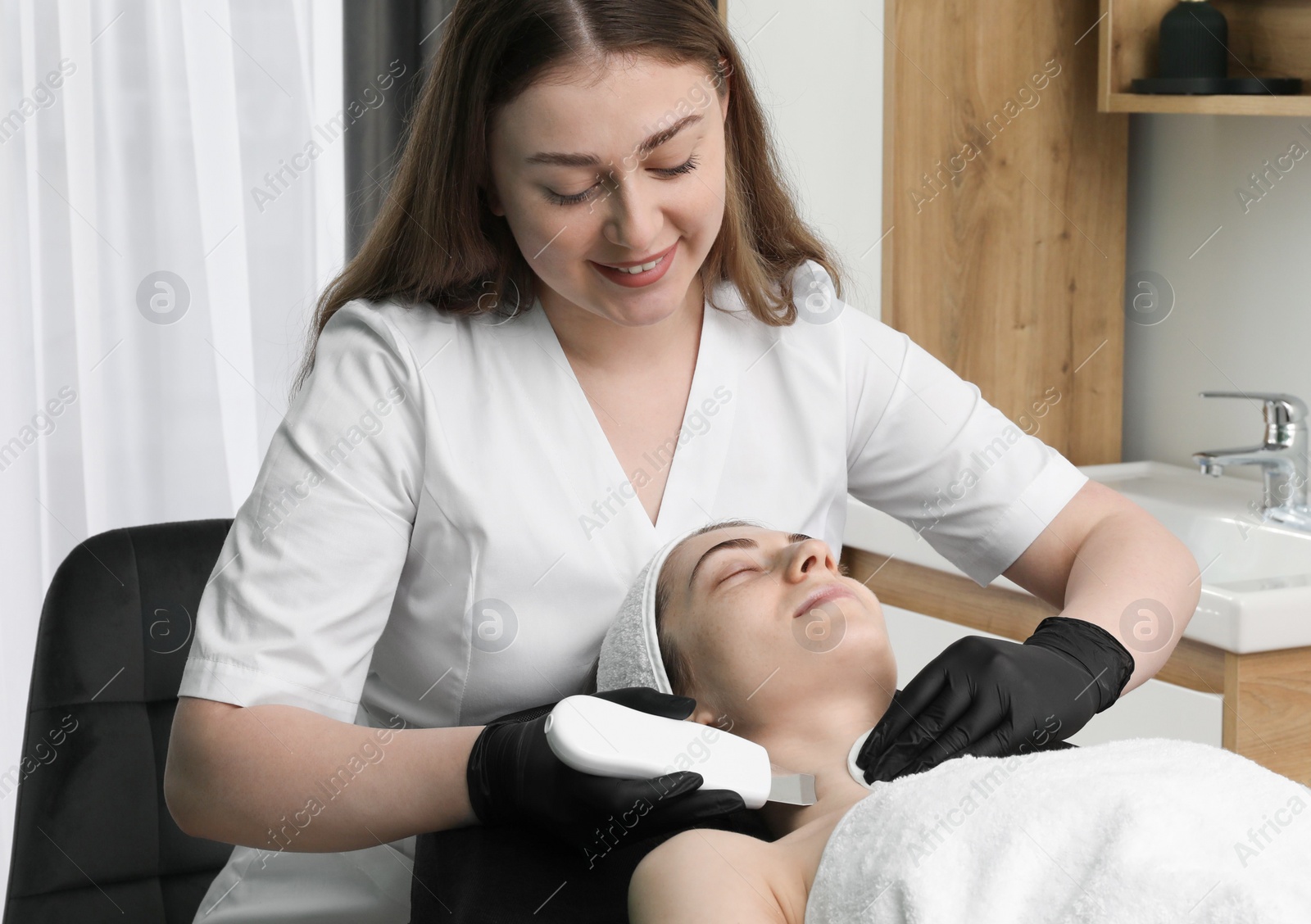 Photo of Cosmetologist using ultrasonic scrubber. Client having cleansing procedure in clinic