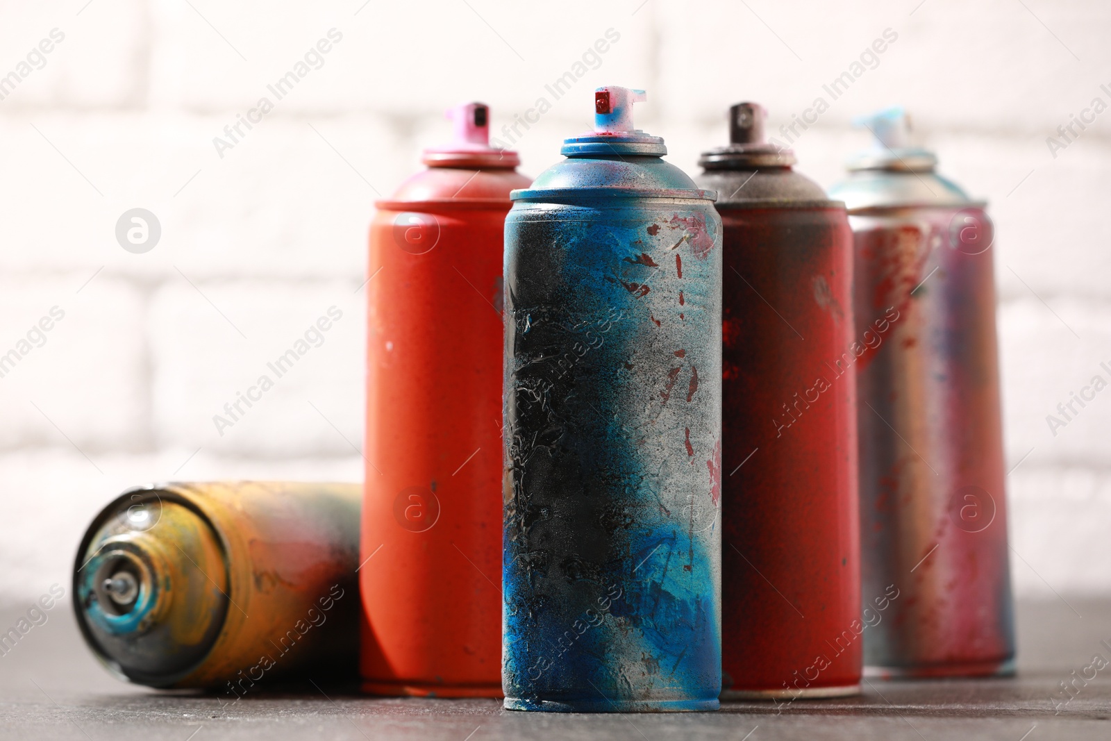 Photo of Many spray paint cans on gray surface against white brick wall, closeup