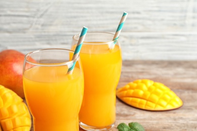 Photo of Fresh tropical mango juice and fruits on wooden table. Space for text