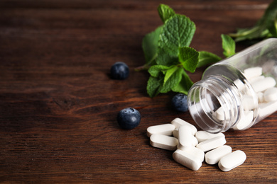 Photo of Bottle with vitamin pills and blueberries on wooden table. Space for text
