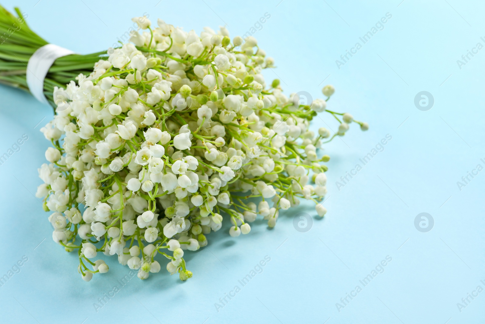 Photo of Beautiful lily of the valley bouquet on light blue background, closeup. Space for text