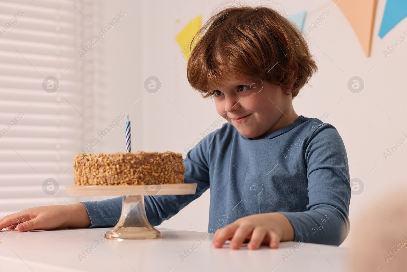 Photo of Cute boy with birthday cake at white table indoors