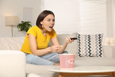 Photo of Surprised woman eating popcorn while watching TV on sofa at home, space for text