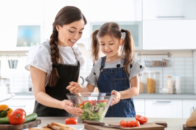 Young nanny with cute little girl cooking together in kitchen