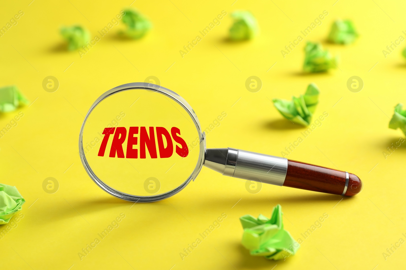 Image of Searching new and popular trends. Magnifier glass with word and green crumpled paper balls on yellow background, closeup