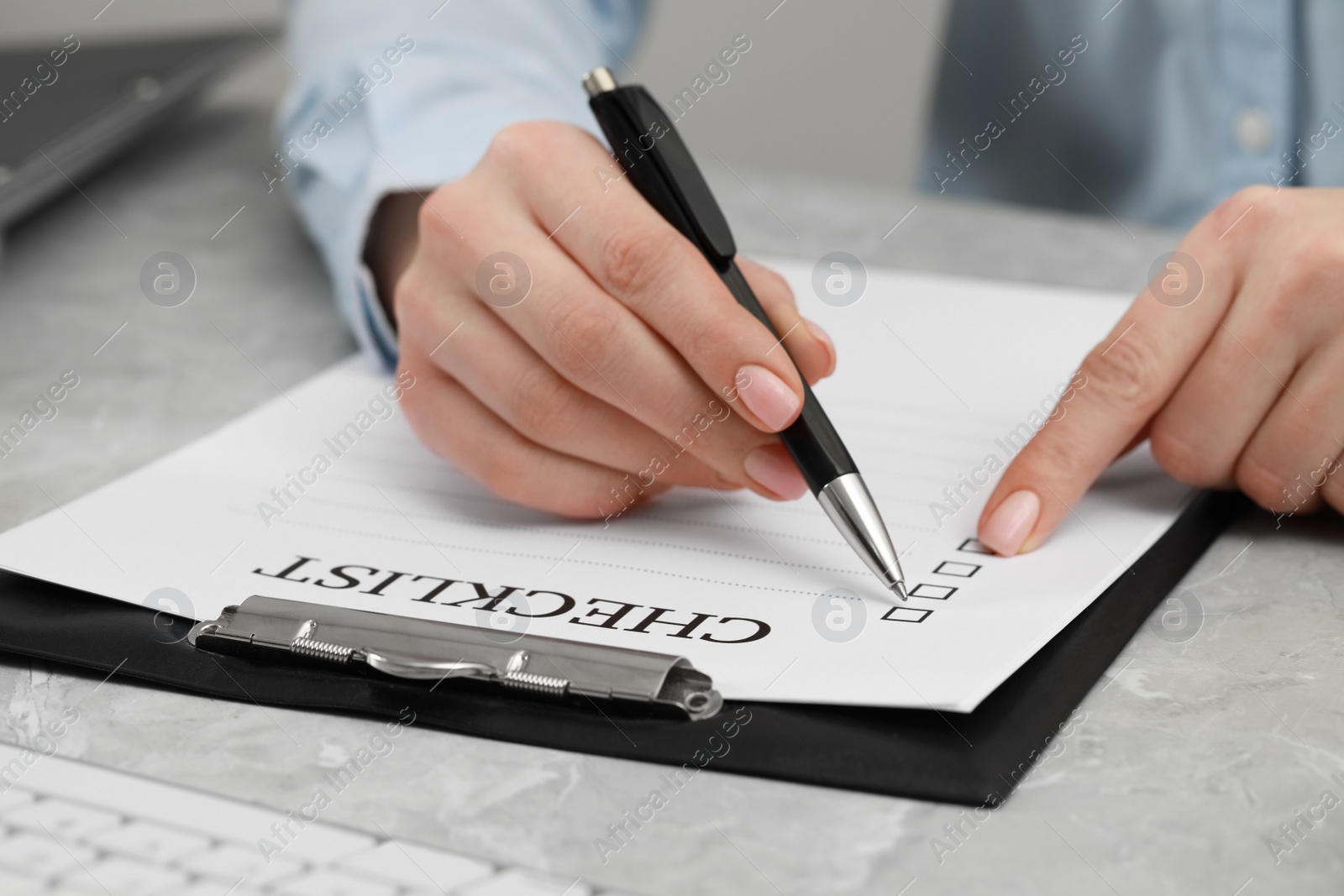 Photo of Woman filling Checklist at grey marble table, closeup