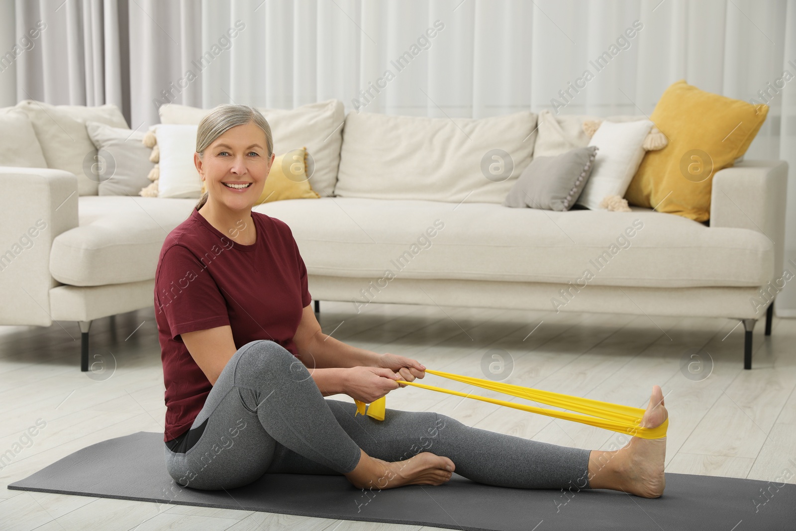 Photo of Senior woman doing exercise with fitness elastic band on mat at home