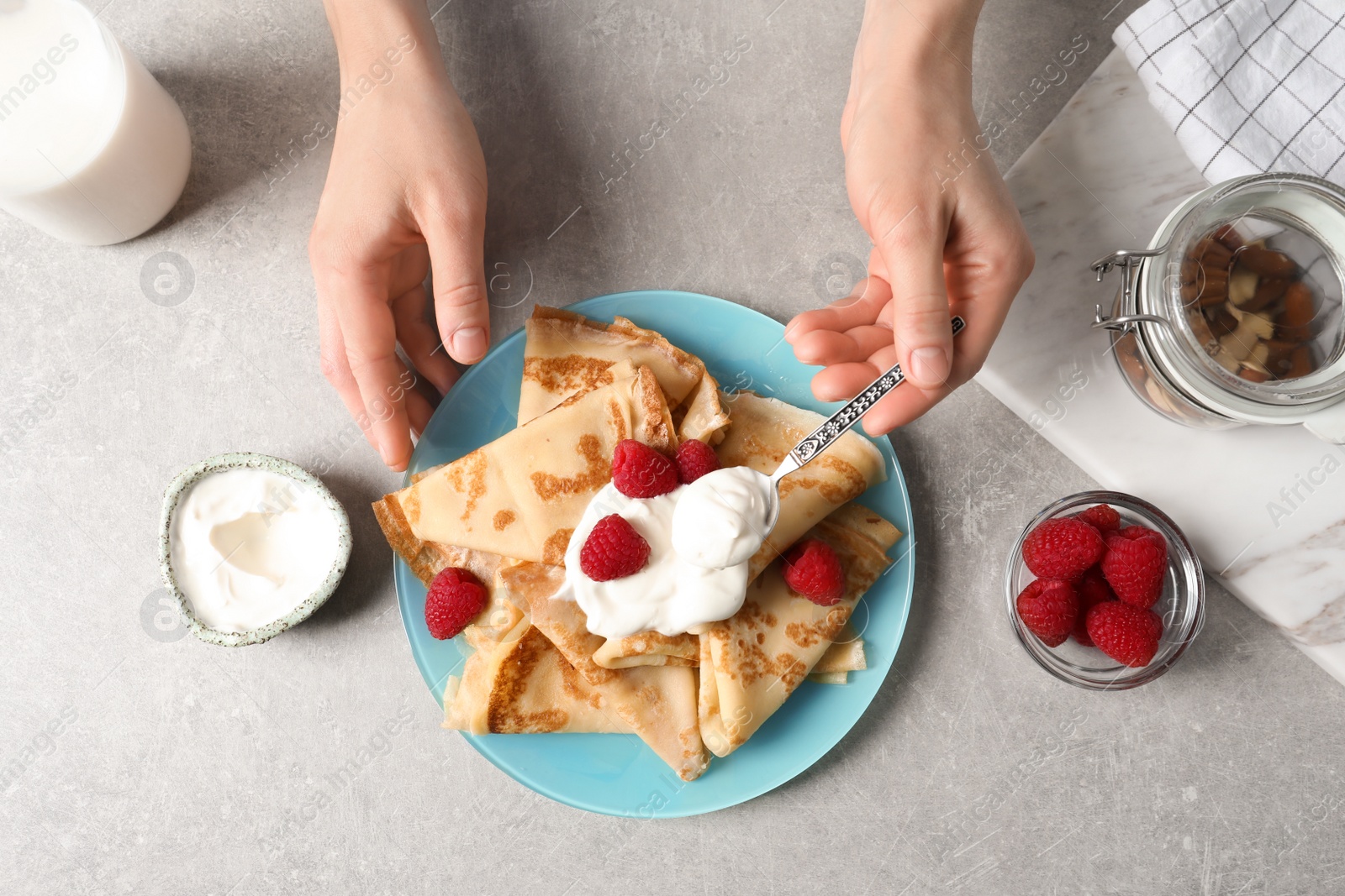 Photo of Woman adding sour cream to thin pancakes with berries at table, top view