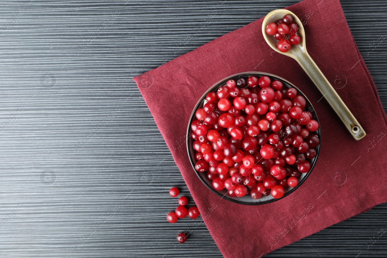 Photo of Cranberries in bowl and spoon on black wooden table, top view. Space for text