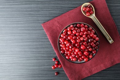 Photo of Cranberries in bowl and spoon on black wooden table, top view. Space for text