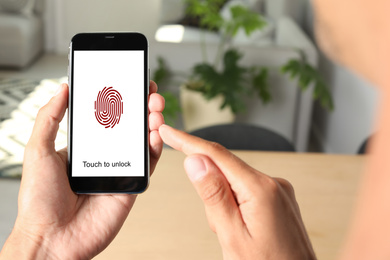Image of Man holding smartphone with fingerprint sensor indoors, closeup. Digital identity