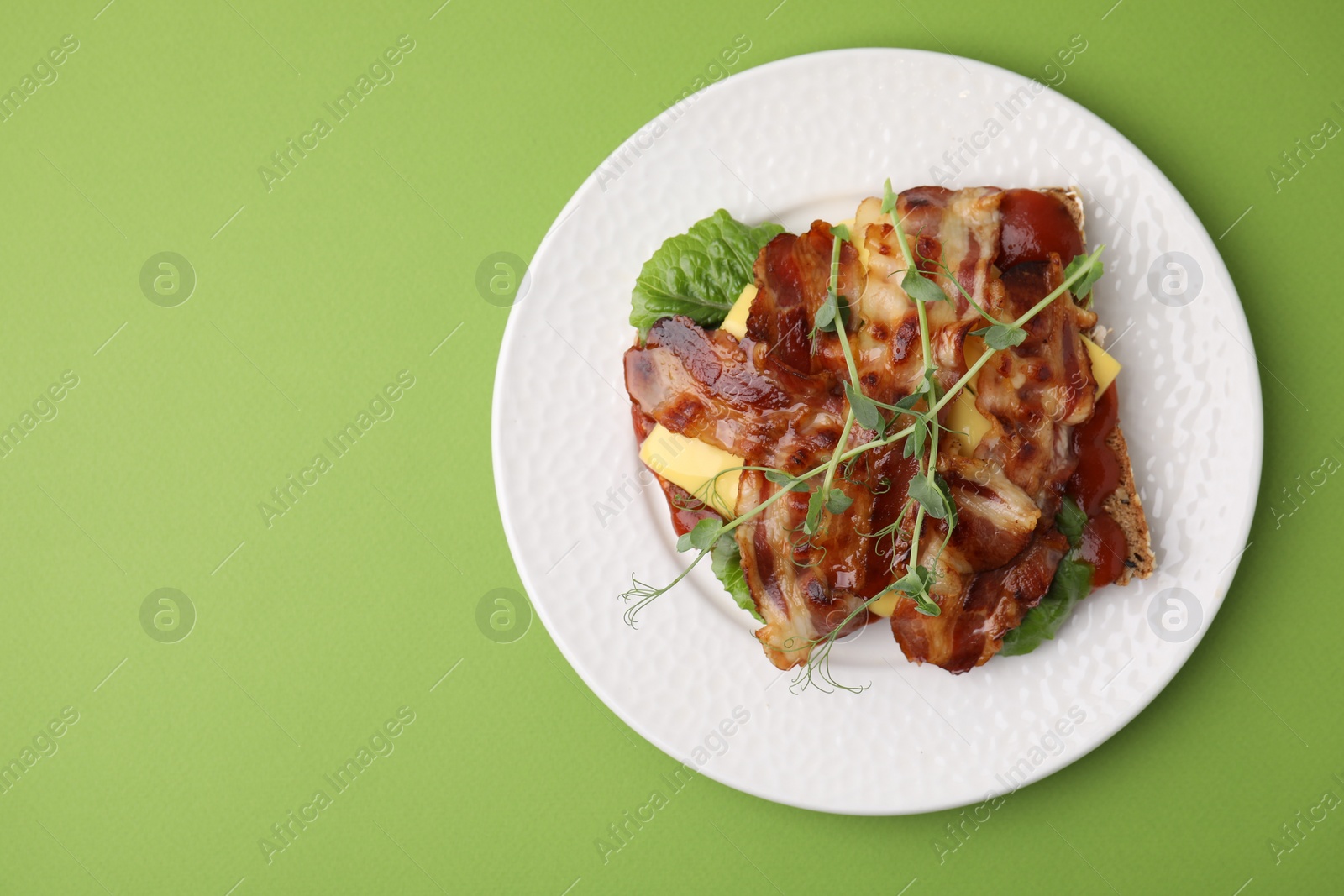 Photo of Tasty sandwich with bacon and microgreens on green table, top view. Space for text