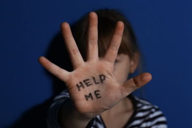 Abused little girl showing with phrase HELP ME near blue wall, focus on hand. Domestic violence concept