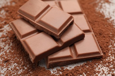 Photo of Delicious milk chocolate and cocoa powder on table, closeup