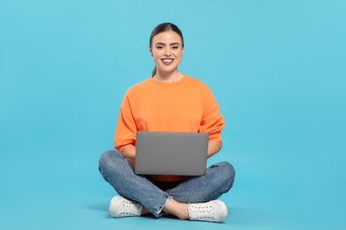 Photo of Happy woman in headphones using laptop on light blue background