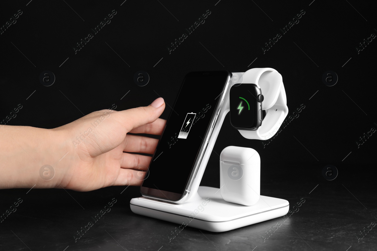 Photo of Woman putting mobile phone onto wireless charger at  black stone table, closeup