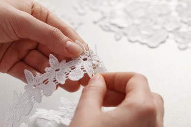 Dressmaker working with beautiful white lace at table in atelier, closeup