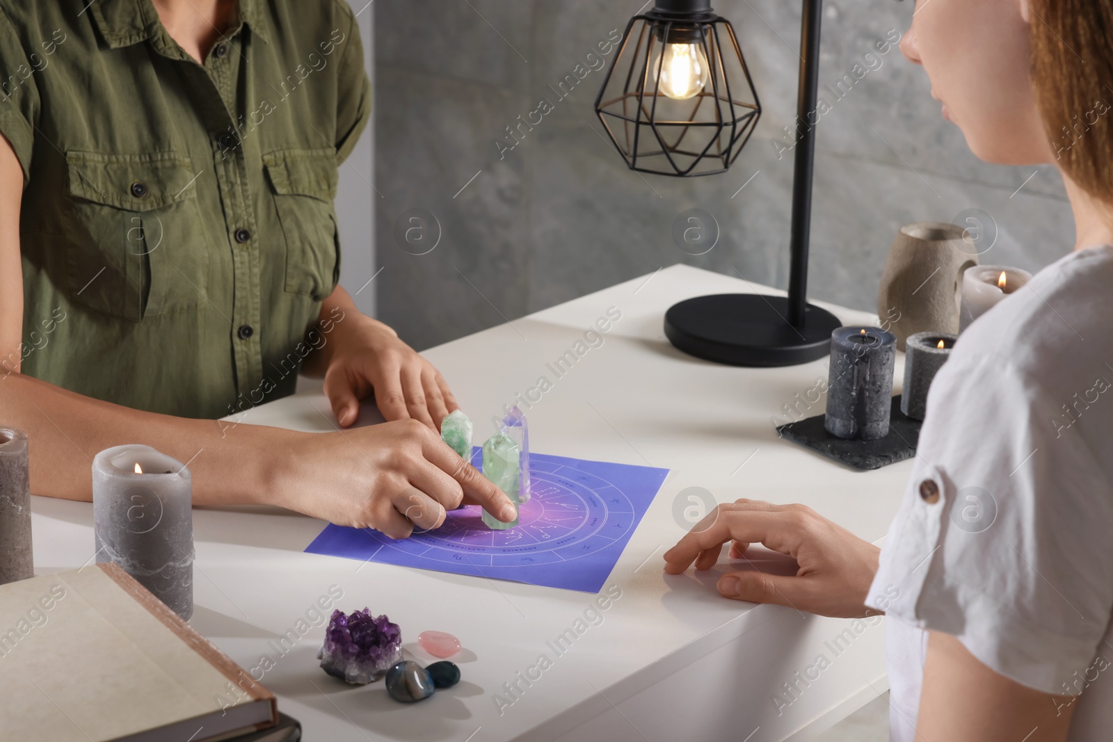 Photo of Astrologer predicting client's future with zodiac wheel and crystals at table indoors, closeup