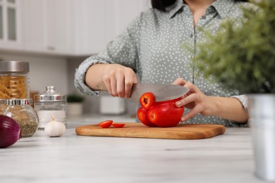 Photo of Cooking process. Woman cutting bell pepper at white countertop in kitchen, closeup