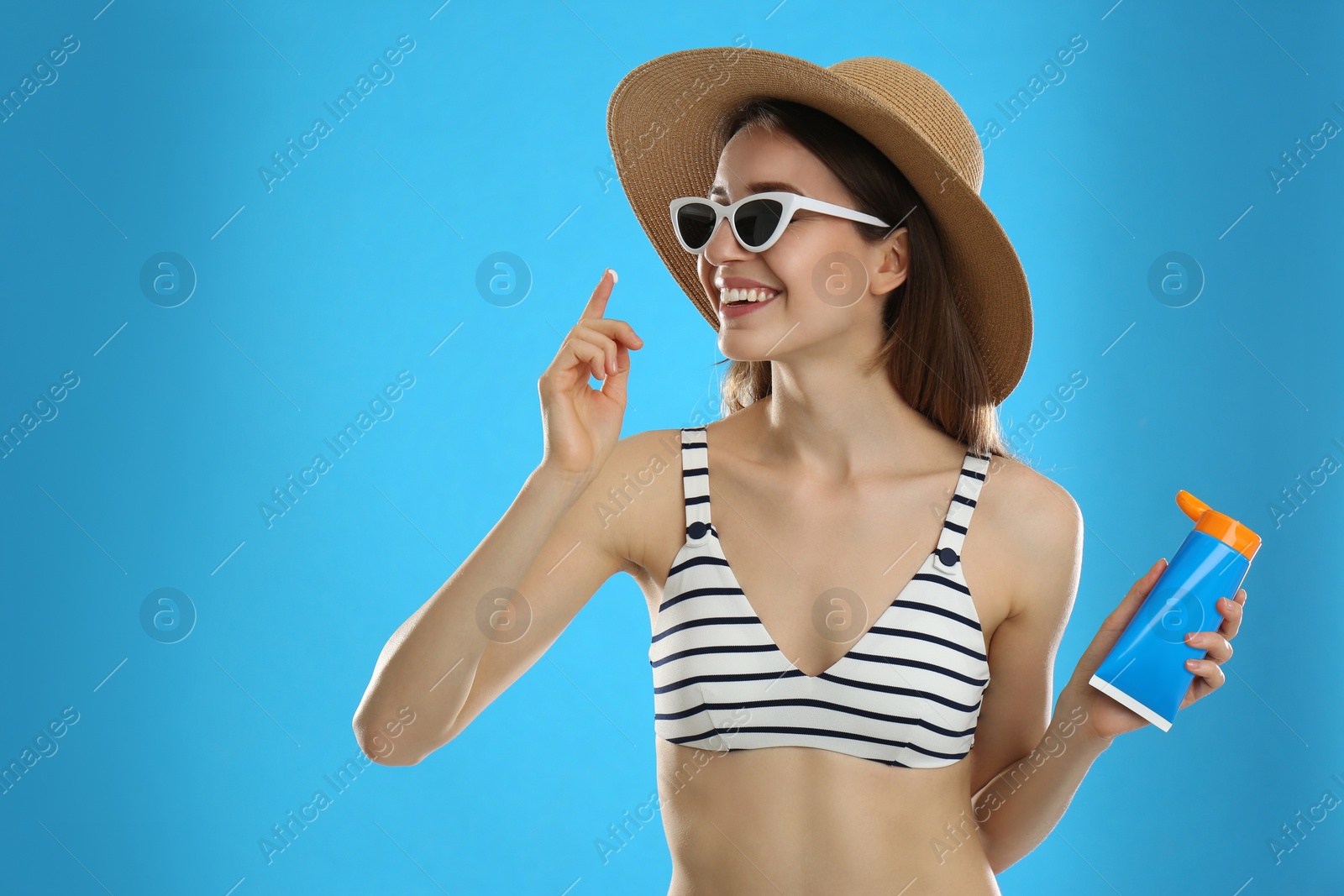 Photo of Young woman applying sun protection cream on light blue background