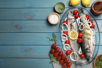 Photo of Glass baking tray with sea bass fish and ingredients on light blue wooden table, flat lay. Space for text