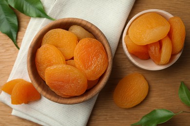 Tasty apricots with bowl on wooden table, flat lay. Dried fruits