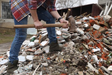 Man with sledgehammer on pile of broken stones outdoors, closeup