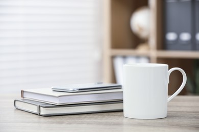 Photo of White ceramic mug and notebooks on wooden table indoors. Space for text