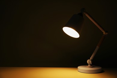 Stylish modern desk lamp on table at night, space for text