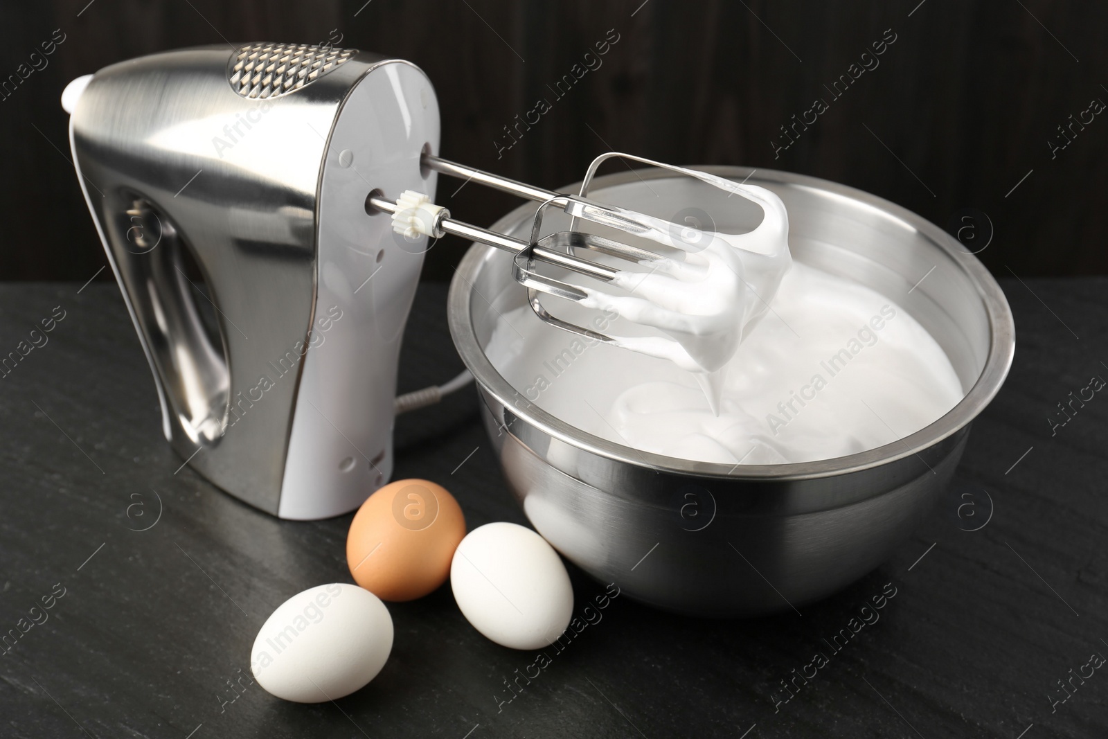 Photo of Bowl with whipped cream, hand mixer and eggs on black table