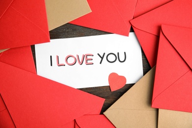 Card with phrase I Love You, red heart and envelopes on wooden table, flat lay