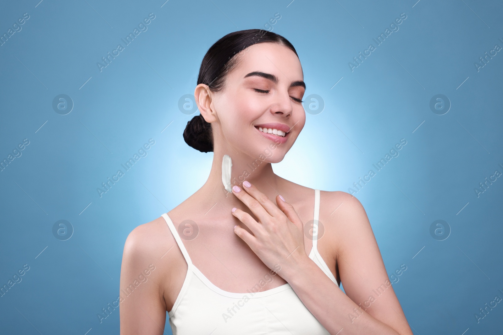 Photo of Beautiful woman with smear of body cream on her neck against light blue background