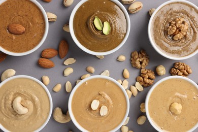 Photo of Many tasty nut butters in bowls and nuts on grey table, flat lay