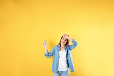 Photo of Woman with air conditioner remote suffering from heat on color background