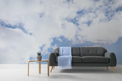 Blue sky with clouds as wallpaper pattern. Living room interior with sofa and side table near wall