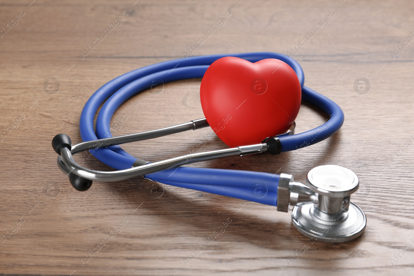 Photo of Stethoscope and red heart on wooden table, closeup. Cardiology concept