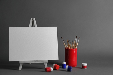 Wooden easel with blank canvas board and painting tools for children on dark background. Space for text