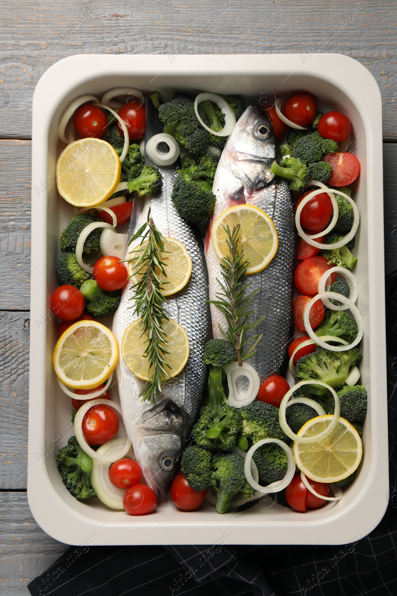 Photo of Raw fish with vegetables and lemon in baking dish on grey wooden table, top view