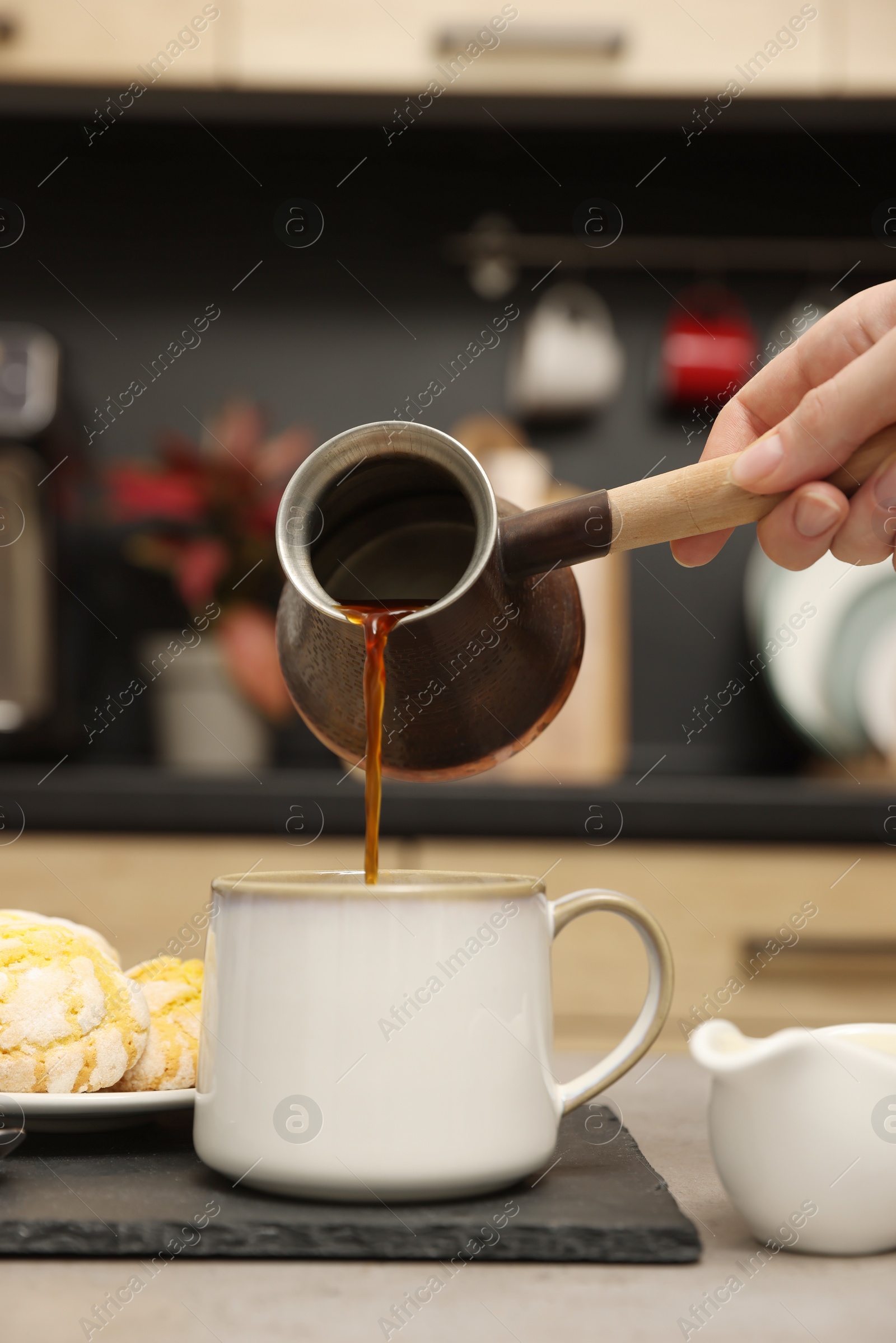 Photo of Woman pouring coffee from jezve into cup at table indoors, closeup. Turkish coffee