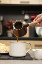 Woman pouring coffee from jezve into cup at table indoors, closeup. Turkish coffee