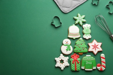 Photo of Kitchen utensils near Christmas tree shape made of delicious gingerbread cookies on green background, flat lay. Space for text