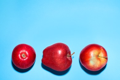 Photo of Ripe red apples on light blue background, flat lay. Space for text