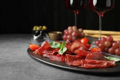 Photo of Delicious bresaola, tomato and basil leaves on grey textured table. Space for text