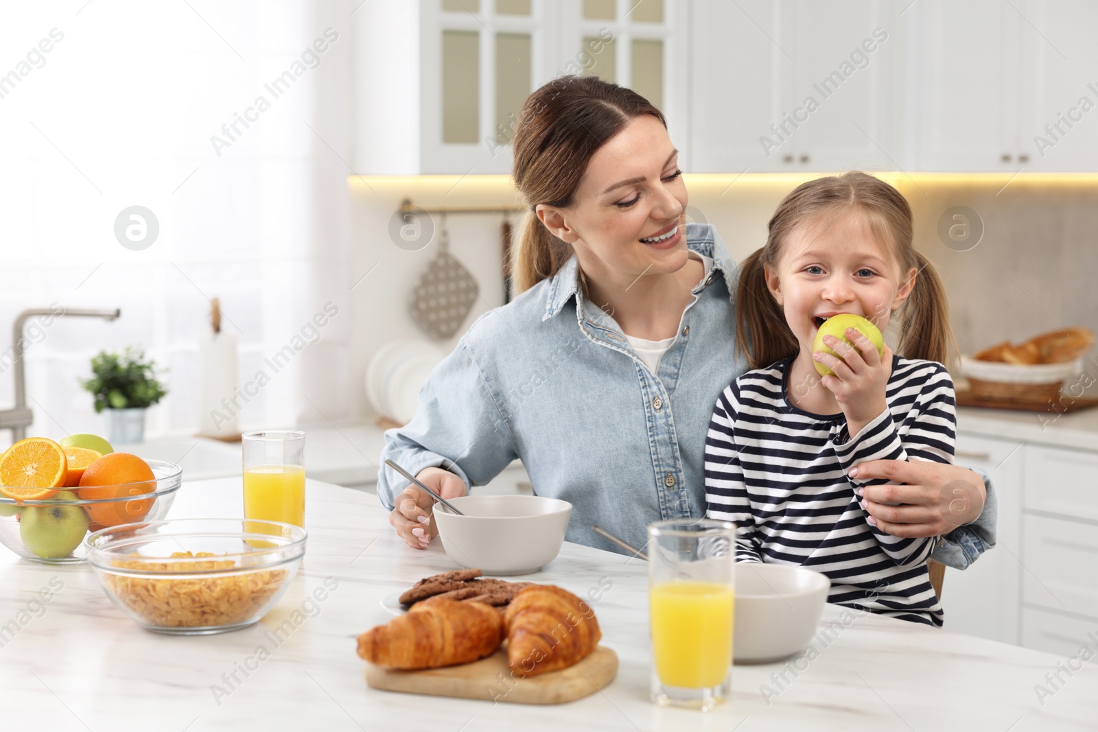 Photo of Mother and her cute little daughter having breakfast at table in kitchen
