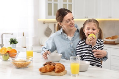 Photo of Mother and her cute little daughter having breakfast at table in kitchen