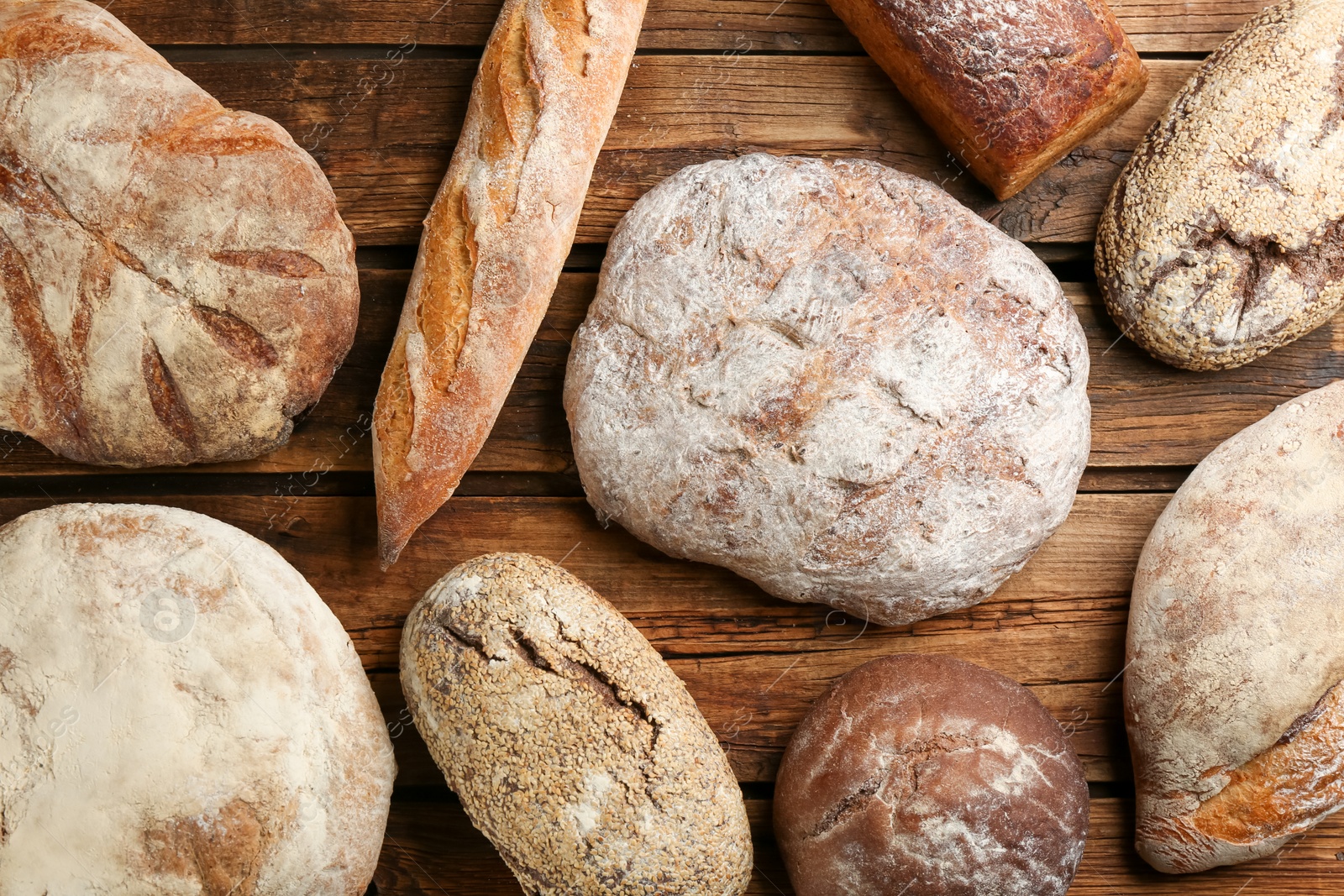 Photo of Different kinds of fresh bread on wooden table, flat lay