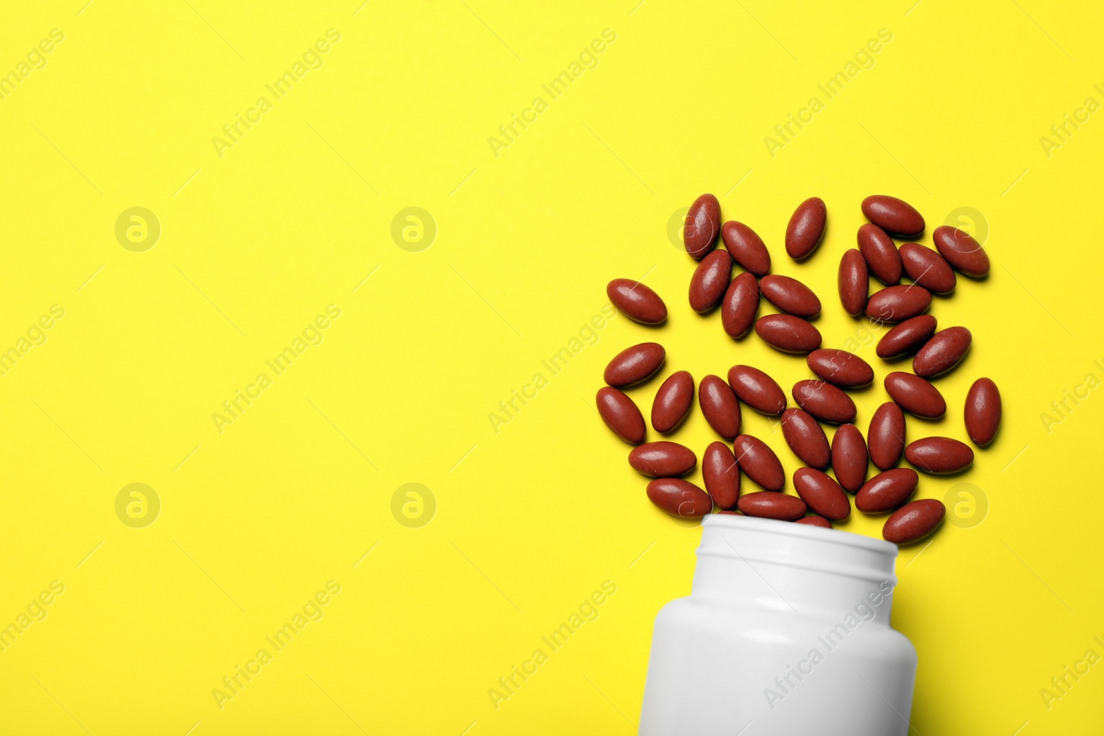 Photo of Bottle with pills on yellow background, flat lay. Space for text